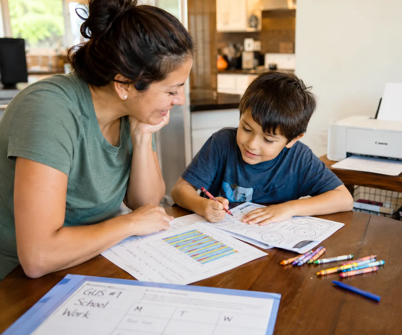 A caregiver smiling beside a child coloring a printable worksheet at a kitchen table.